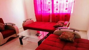 A living room with a red sofa set, a glass coffee table, and a red curtain with floral patterns. - Residence Perle de L'Atlas 4608 (Marrakech)