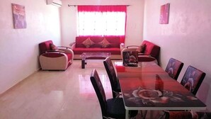 A living room with a red sofa, a coffee table, and a dining table with chairs. - Residence Perle de L'Atlas 4608 (Marrakech)