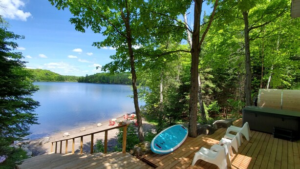 Une terrasse en bois avec une piscine, des chaises blanches et une vue sur un lac entouré d’arbres.
