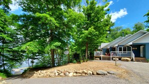 Une cabane avec une allée en gravier, une véranda dotée de meubles d’extérieur et une vue sur un lac.