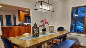 Un coin repas avec une table en bois, des chaises bleues et un banc. On y trouve deux lanternes et un vase rempli de fleurs sur la table.