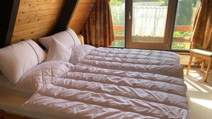 A bed with a quilted cover and pillows, wooden headboard, and a window with curtains.