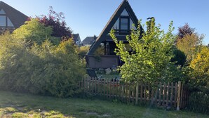 A house with a triangular roof, surrounded by a wooden fence and lush greenery.