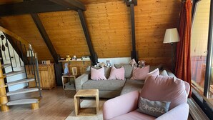 A cozy loft-style room with a wooden ceiling, a staircase, a sofa set, and a small wooden table.