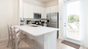 A modern kitchen with white cabinetry, stainless steel appliances, and a central island with seating. - Sunny Margaritaville Cottage - Fully Equipped Kitchen, Welcoming Living Area (Kissimmee)