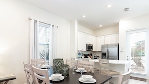 A modern kitchen with white cabinets, stainless steel appliances, and a dining area with a dark wooden table and light-colored chairs. - Sunny Margaritaville Cottage - Fully Equipped Kitchen, Welcoming Living Area (Kissimmee)