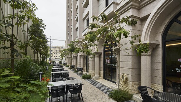 An outdoor cafe area with tables and chairs, surrounded by greenery and a checkered floor. - Menippe Hotel (Kaohsiung)