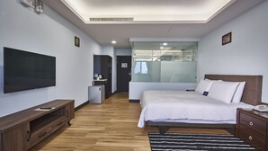 A modern hotel room with a large bed, a flat-screen TV, a wooden entertainment unit, and a glass shower enclosure. - Menippe Hotel (Kaohsiung)