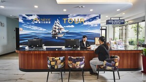 A hotel reception desk with a large 'TOUR' sign, a computer, and a reception area with chairs. - Menippe Hotel (Kaohsiung)