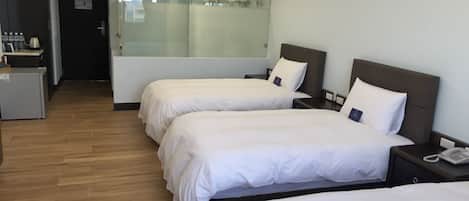 A hotel room with two beds, a small desk, and a glass partition separating the room from a bathroom.