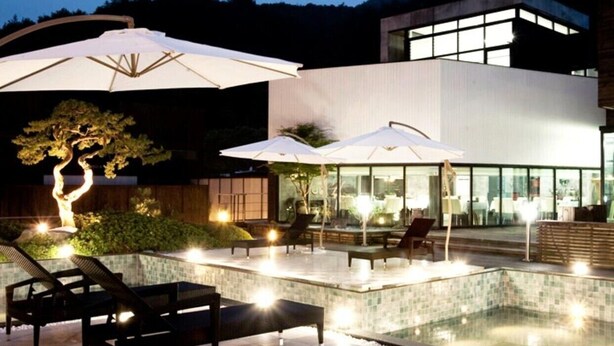 A modern outdoor pool area with lounge chairs and umbrellas, surrounded by a building with large windows.