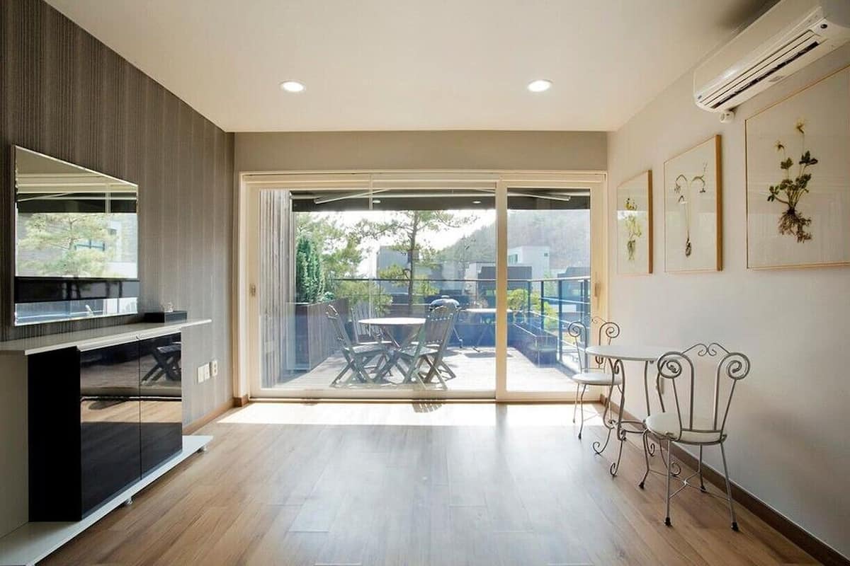 Sala de estar moderna com porta de vidro deslizante para uma varanda, área de jantar com cadeiras de metal e ar-condicionado instalado.