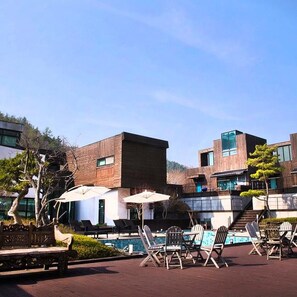 Un espace piscine extérieur moderne, doté de chaises longues et de parasols, et entouré de bâtiments contemporains aux grandes fenêtres.