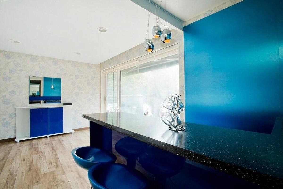 Cozinha moderna com parede azul, uma janela grande e área de bar com banquetas.