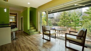 A modern kitchen with a dining area, a staircase, and large windows offering a view of greenery.