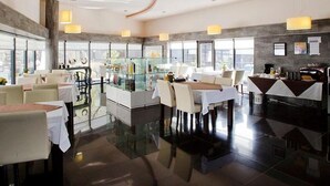 A modern restaurant with a glass partition, white tables, and a bar area.