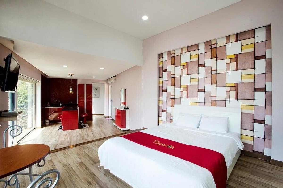 Quarto de hotel com cama, escrivaninha e cozinha compacta.