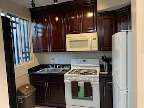 A compact kitchen with dark wooden cabinets, a white stove, a microwave, and a refrigerator. - Casa de los Sueños only 10 to 15 minutes away from the beach or downtown (Puerto Peñasco)