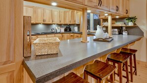A kitchen with wooden cabinets, a granite countertop, and bar stools. - SHADE MOUNTAIN RETREAT ★ CEDAR BARREL SAUNA & HOT TUB!! ★ 28 ACRES ★ SLEEPS 20 (East Waterford)
