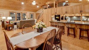 A spacious kitchen with wooden cabinets, a dining area with a table and chairs, and a staircase leading to an upper level. - SHADE MOUNTAIN RETREAT ★ CEDAR BARREL SAUNA & HOT TUB!! ★ 28 ACRES ★ SLEEPS 20 (East Waterford)