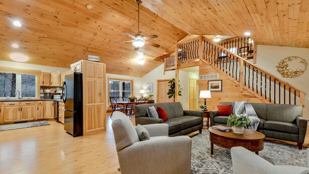 A spacious living area with a wooden ceiling, a staircase, and a kitchen with wooden cabinets. - SHADE MOUNTAIN RETREAT ★ CEDAR BARREL SAUNA & HOT TUB!! ★ 28 ACRES ★ SLEEPS 20 (East Waterford)