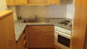 Una pequeña cocina con armarios de madera, encimera de granito, pileta de acero inoxidable y estufa blanca.