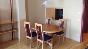 Un comedor con una mesa redonda de madera, cuatro sillas con cojines oscuros, una lámpara colgante blanca y un mueble de madera sobre la mesa.