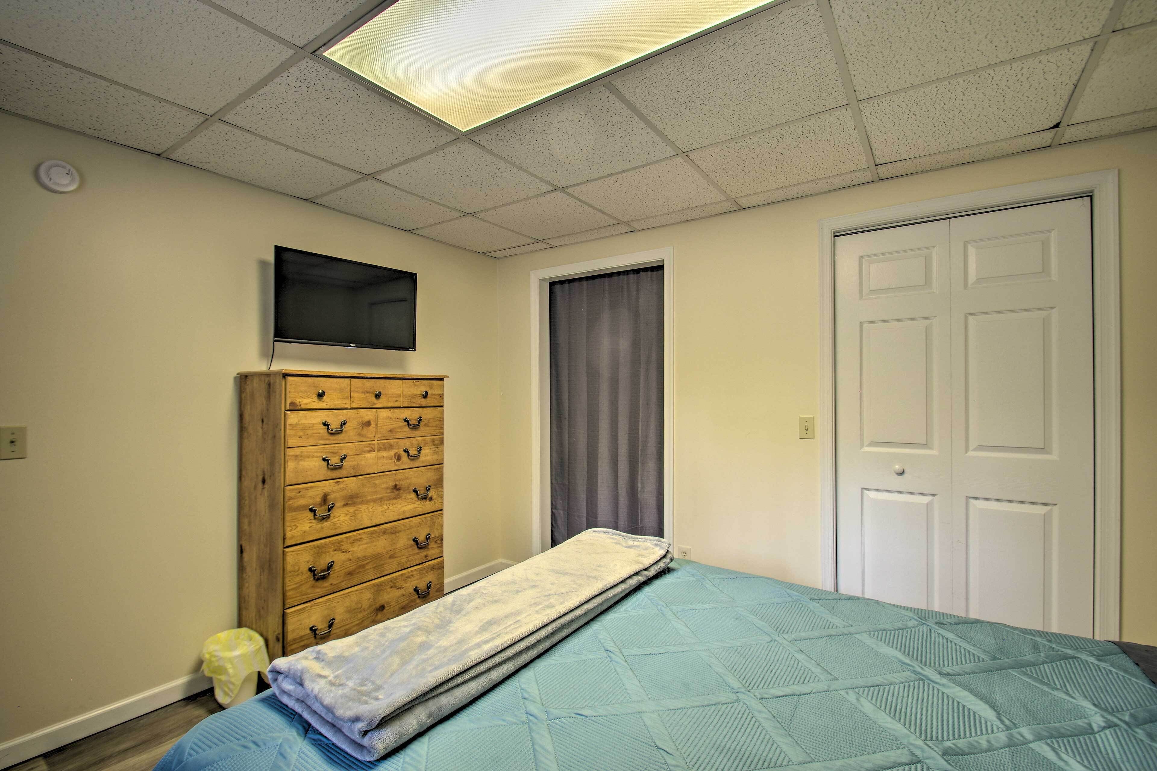 Een slaapkamer met een bed, een houten dressoir, een televisie aan de muur en een deur.