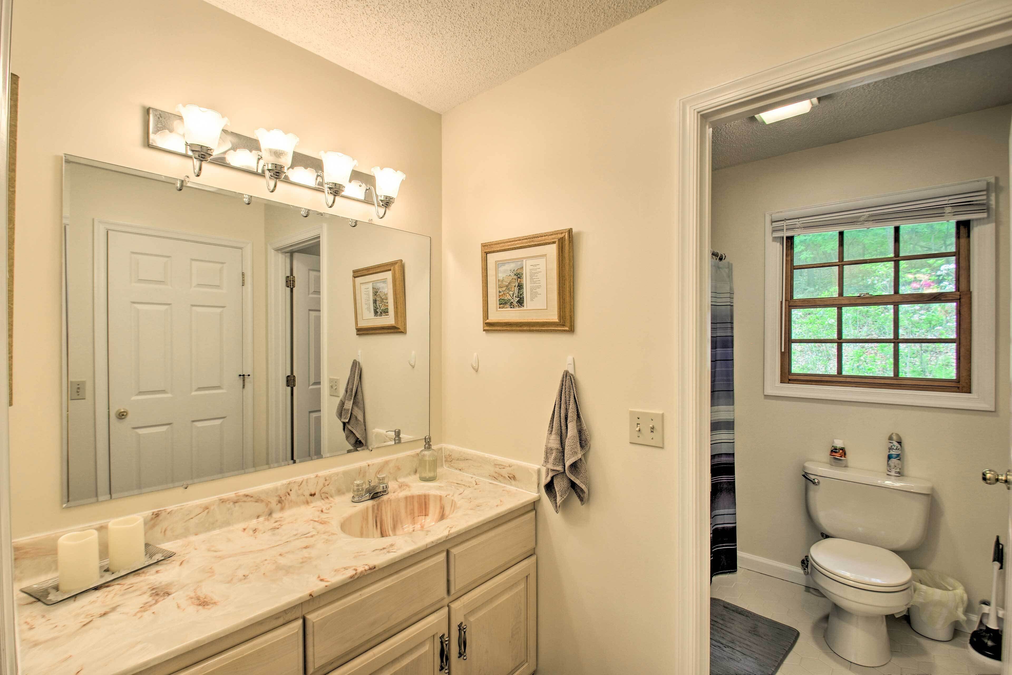 A bathroom with a marble sink, a large mirror, a framed picture on the wall, and a window with blinds.