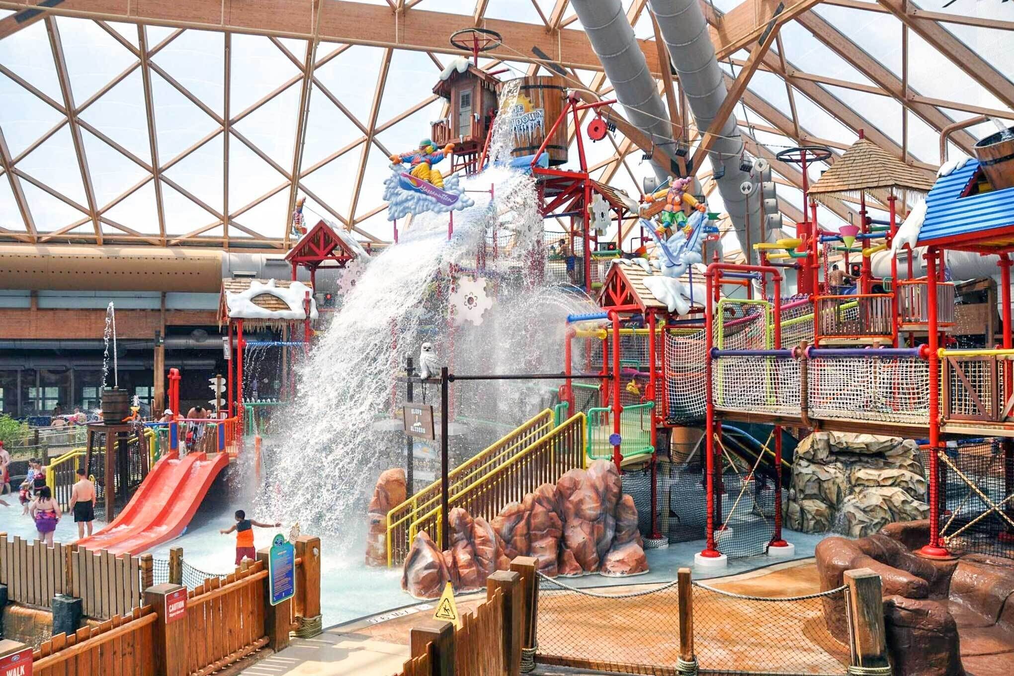 Een overdekt waterpark met glijbanen, fonteinen en speelconstructies.