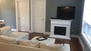 Sala de estar com sofá branco, lareira e televisão montada acima.