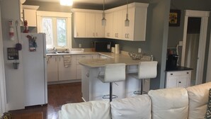 Cozinha moderna com armários brancos, uma ilha central com banquetas e uma geladeira com ímãs, além de micro-ondas.