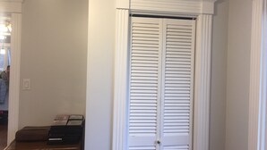 Uma porta branca com detalhes decorativos, um banco de madeira com uma pequena mesa ao lado e um interruptor de luz na parede.