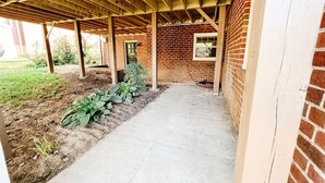 A covered patio area with a brick wall, wooden beams, and a concrete floor. - Steps to Lane And VT Campus Cozy 2 bed/2 bath Blacksburg Apartment (Blacksburg)