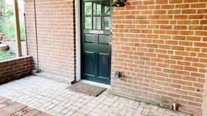 A brick building with a green door labeled "WELCOME," a small outdoor area with a brick floor, and a wall-mounted light fixture. - Steps to Lane And VT Campus Cozy 2 bed/2 bath Blacksburg Apartment (Blacksburg)