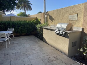 Een terras buiten met een barbecue, een tafel met stoelen en een bord aan de muur.