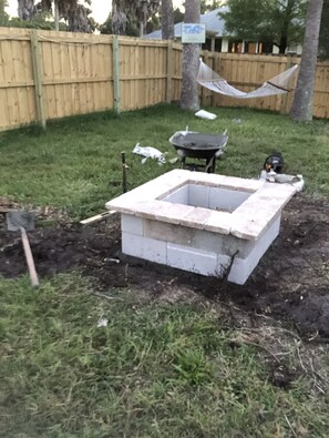 Ein Garten mit einer Betonkonstruktion, einem Holzzaun, einer Hängematte und einem Rasenwagen.
