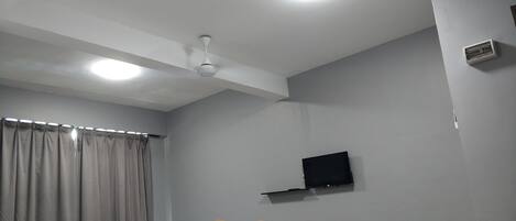 A modern living room with a flat-screen TV mounted on the wall, a ceiling fan, and a dining area with a table and chairs.