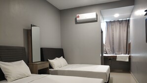 A hotel room with two beds, a bedside table, a mirror, an air conditioning unit, a window with curtains, and a sink with a towel. - Reno Rooms Ipoh (Ipoh)