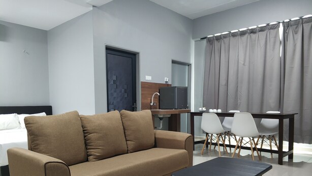A modern hotel room with a brown sofa, a small black table, and a dining area with white chairs. - Reno Rooms Ipoh (Ipoh)