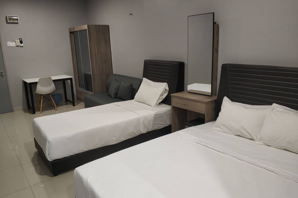 A hotel room with two single beds, a desk, a chair, a wardrobe, and a large mirror.