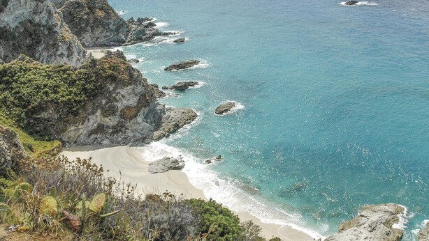 Un paisaje costero con acantilados rocosos, aguas turquesas cristalinas y una playa de arena.
