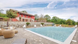 Un área de piscina con sillones de descanso, un muro de piedra y un edificio rojo al fondo.