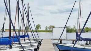 A wooden dock leading to a row of boats with masts, docked at a calm body of water.