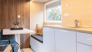 A modern kitchen with white cabinets, a wooden accent wall, a window with blinds, and a built-in bench with cushions.