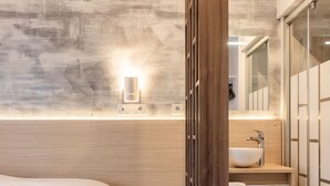A modern bedroom with a large bed, a wooden wardrobe, a built-in sink, and a mirror.
