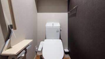 A compact bathroom with a toilet, a small shelf, and a toilet paper holder.