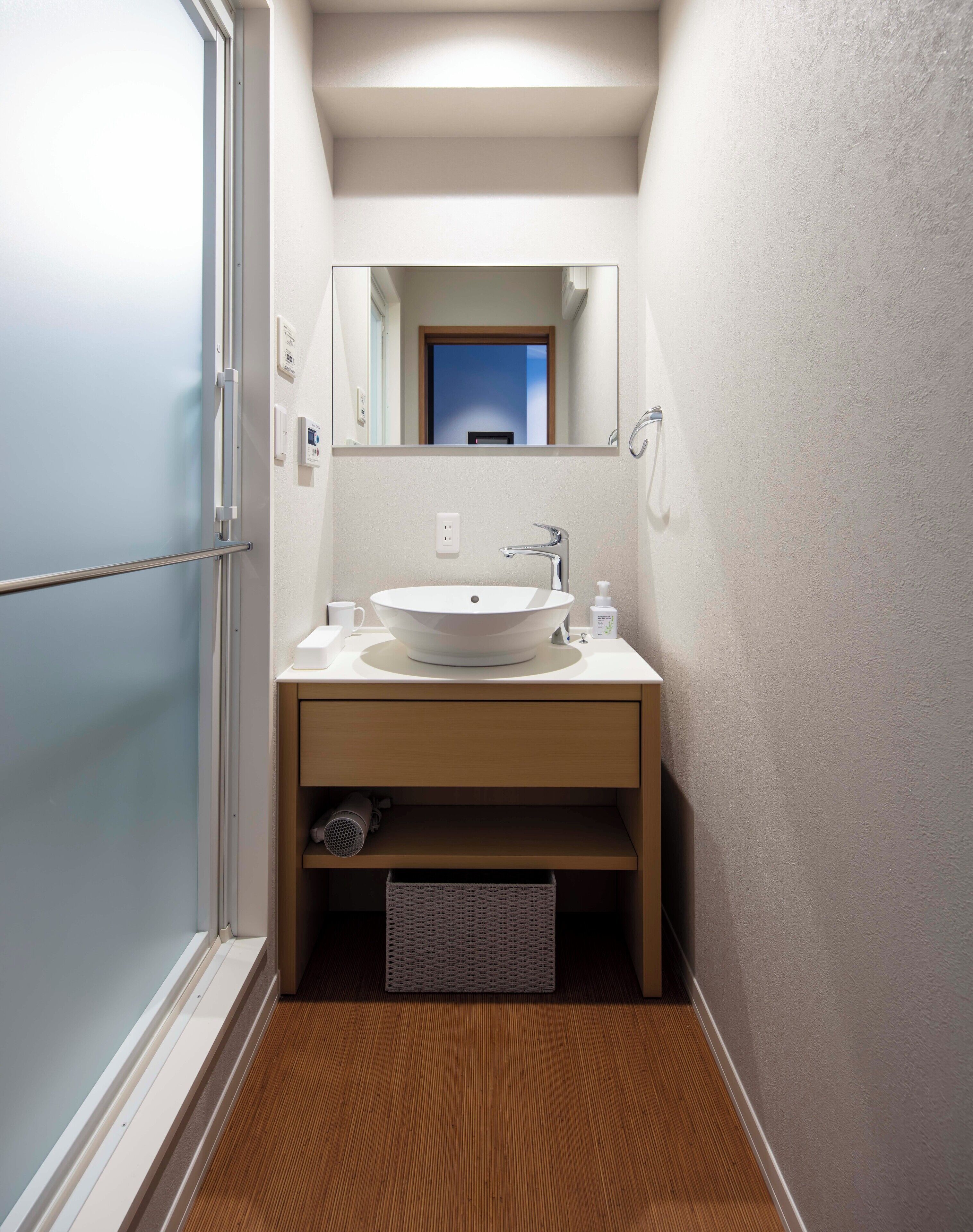 A narrow bathroom with a white sink, a mirror, and a wooden floor.