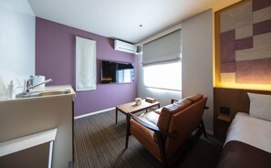 A hotel room with a bed, a desk, a chair, a window with blinds, a flat-screen TV mounted on the wall, and a small table with a vase of flowers. - Grand Base Kurashiki Chuo (Kurashiki)