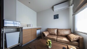 A compact hotel room with a kitchenette, a leather sofa, a wooden coffee table, and a small plant.